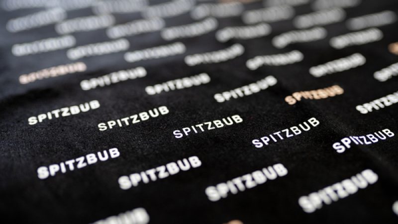 Dieses Bild zeigt das Spitzbub-Logo auf schwarzem Stoff