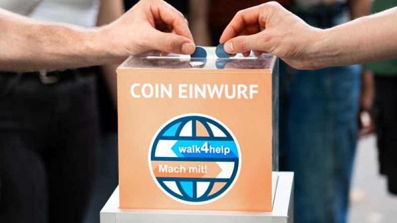 Hände die Münzen in eine Box mit der Beschriftung "Coin Einwurf" stecken.